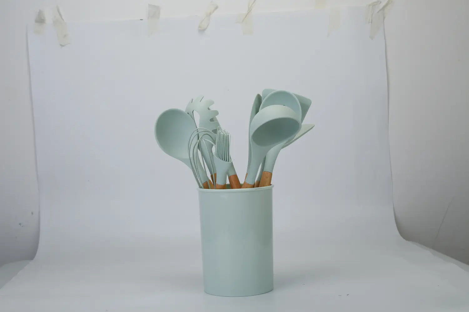 Light blue silicone-coated cooking utensil set with wooden handles neatly arranged in a matching cylindrical holder.