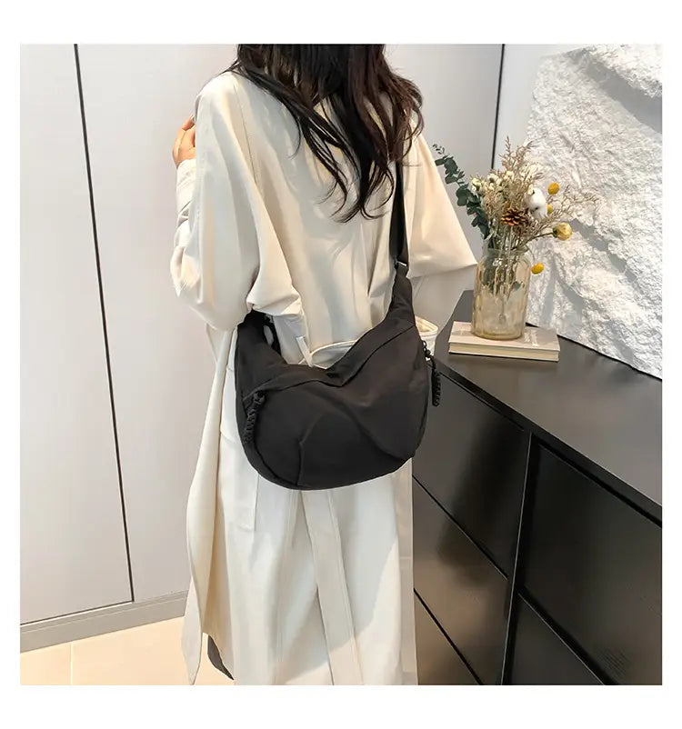 Black nylon crossbody bag with large capacity and sleek curved design featuring subtle zipper details for minimalist style.
