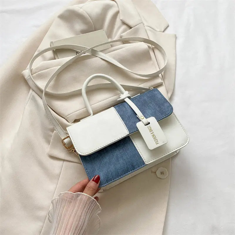 A stylish two tone denim patchwork crossbody bag featuring a white leather flap and denim blue panels accented with gold hardware.