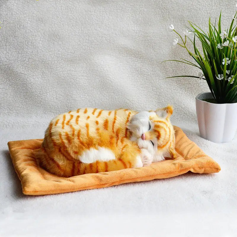 Realistic breathing plush cat figurine in orange and white stripes sleeping on a soft golden brown pet bed cushion.