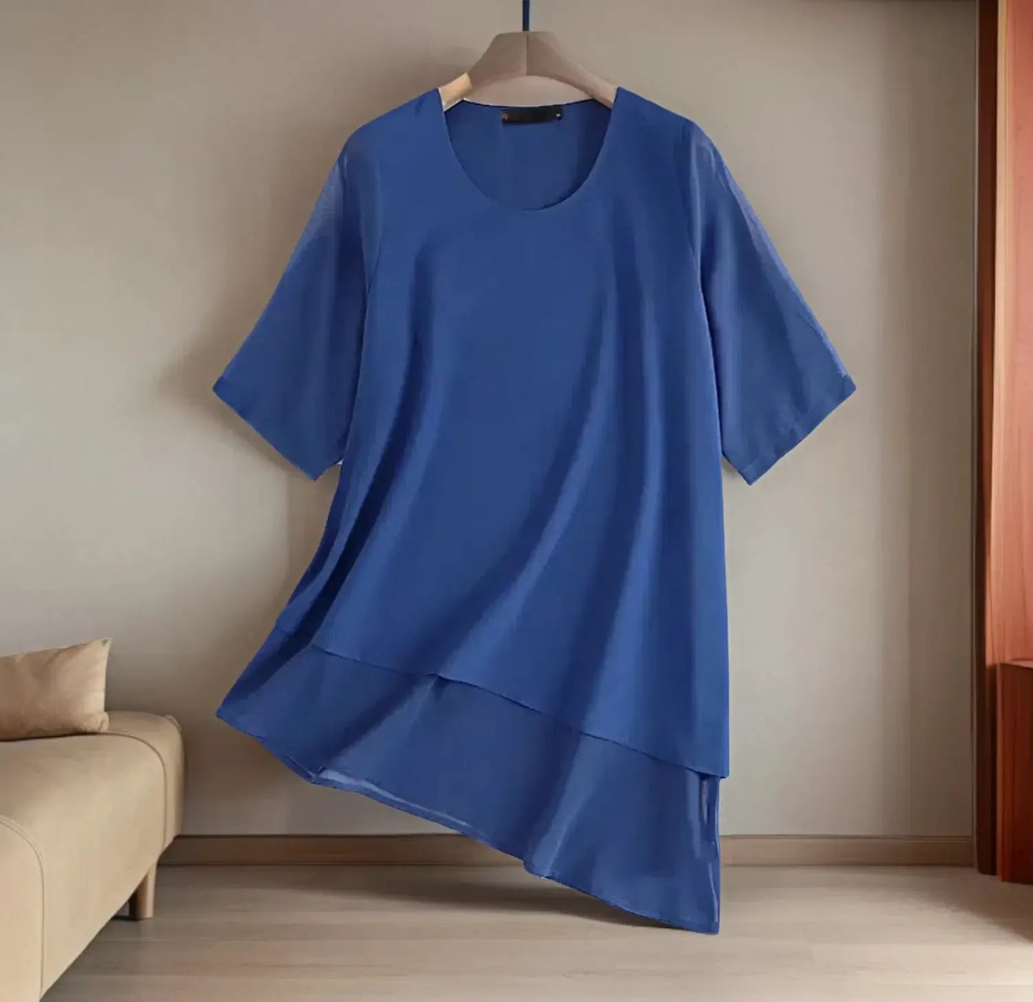A flowing blue chiffon layered plus size tunic with short sleeves and a relaxed fit hanging on a wooden hanger.