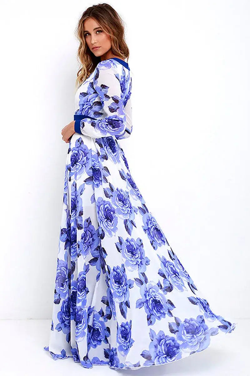 A flowing white maxi dress with a vibrant blue floral pattern, long sleeves, a v-neck, navy trim, and a matching blue belt at the waist.