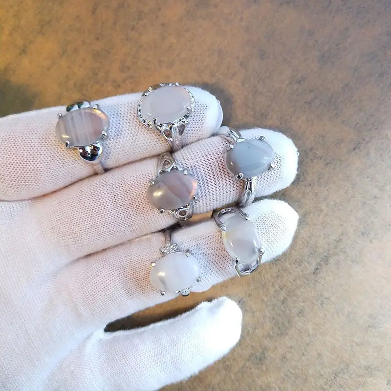 A collection of five elegant natural gemstone silver tone statement rings each featuring a smooth oval-shaped moonstone set in a delicate silver-toned metal band with intricate detailing.