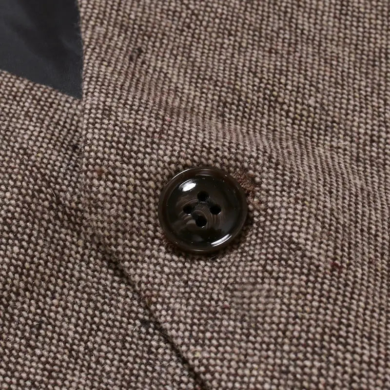 Ein dunkelglänzender Vierlochknopf, angenäht auf einen strukturierten braunen Tweedstoff, an einer Herren-Tweedweste im Slim-Fit im Business-Casual-Stil.