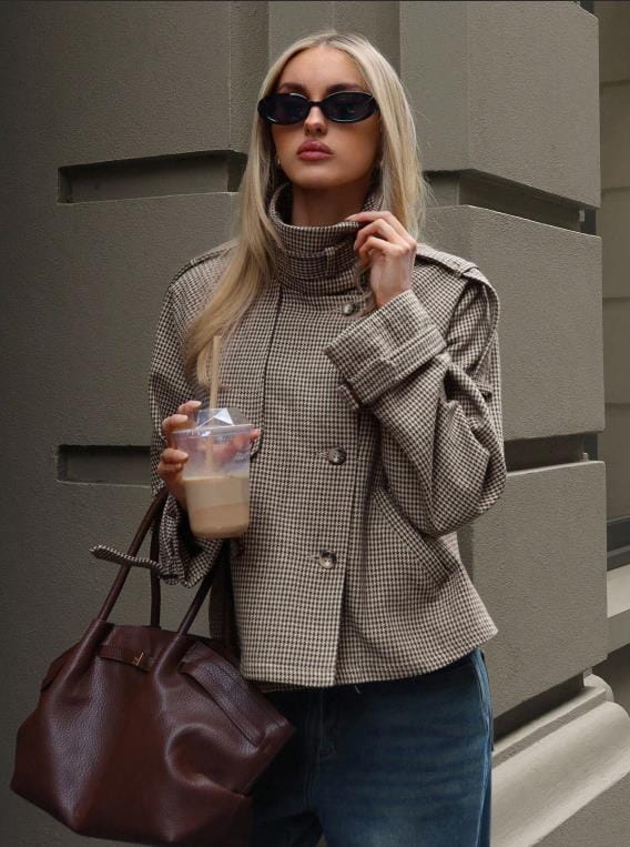 Brown leather handbag with structured shape and top handle displayed alongside a houndstooth coat relaxed fit double breasted jacket.