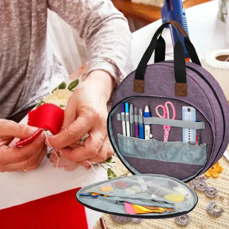 premium circular embroidery and craft tool storage tote in purple fabric with black handles and brown leather-like accents featuring organized compartments for pens scissors rulers and colorful felt pieces.