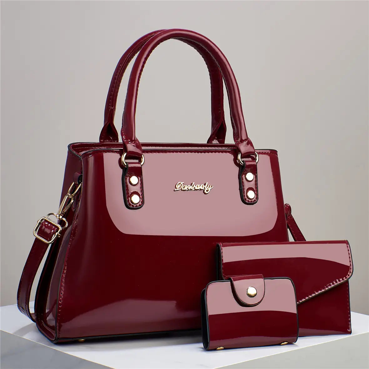 Glossy patent leather 3-piece handbag and wallet set featuring a shiny burgundy patent leather handbag with gold-tone hardware and matching wallet and clutch.