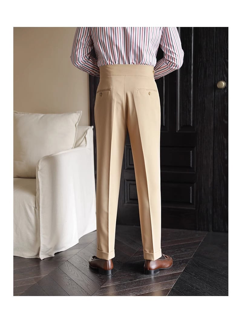 Beige men’s tailored pleated wool straight leg trousers with a high waist and buttoned back pockets shown from the back side.