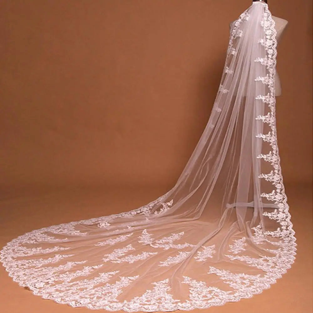 A delicate white embroidered floral lace cathedral wedding veil with comb featuring intricate floral embroidery along the edges and a flowing sheer tulle base.