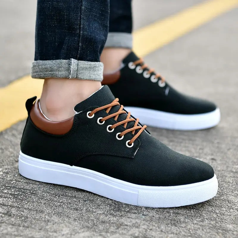Men’s breathable casual sport canvas sneakers in black with brown laces, tan leather heel tab, and white rubber soles shown from the back side.