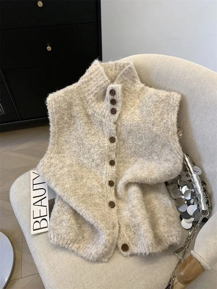 Un cardigan sans manches en maille duveteuse couleur crème, avec un col montant et des boutons bruns issus de la collection gilet tricoté à col haut, boutonné, crème.