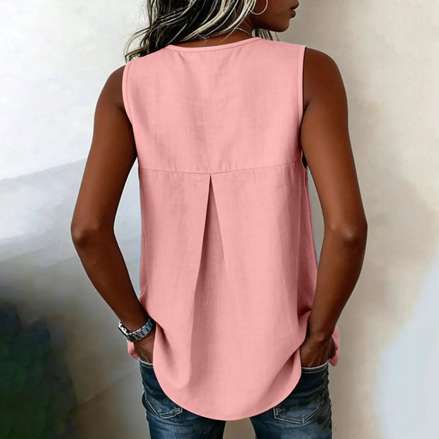 A soft pink sleeveless tie side button down blouse with a relaxed fit and subtle pleated back detail shown from the back side.