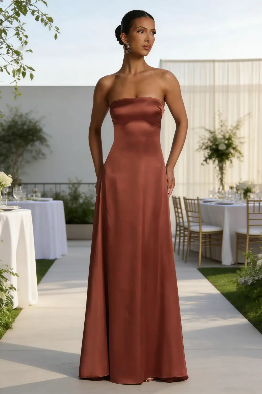 Un elegante vestido de noche sin tirantes de satén satinado en un rico color óxido, con silueta lisa y fluida de largo hasta el suelo y escote drapeado.