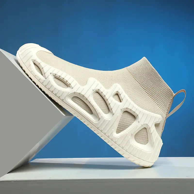 Beiger Strick-Sockensneaker für den Knöchelbereich mit weiß geformter Sohle, versehen mit geometrischen Aussparungen, sowie texturierter Gummiaußensohle aus der Kollektion der Strick-Sockensneaker für Damen und Herren mit geformter Sohle und Freizeit-Schuhen.