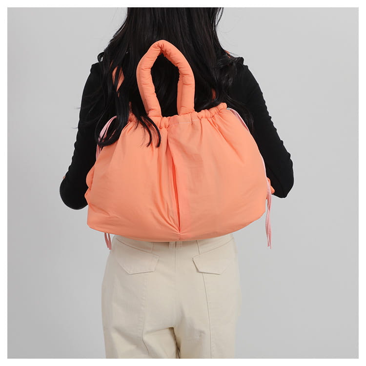 A plush peach-colored quilted puffer tote bag made of lightweight nylon with quilted handles and drawstring ties.