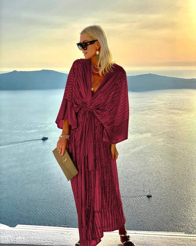 A shimmering burgundy metallic bat sleeve pleated sequin maxi dress with a draped tie-front design.