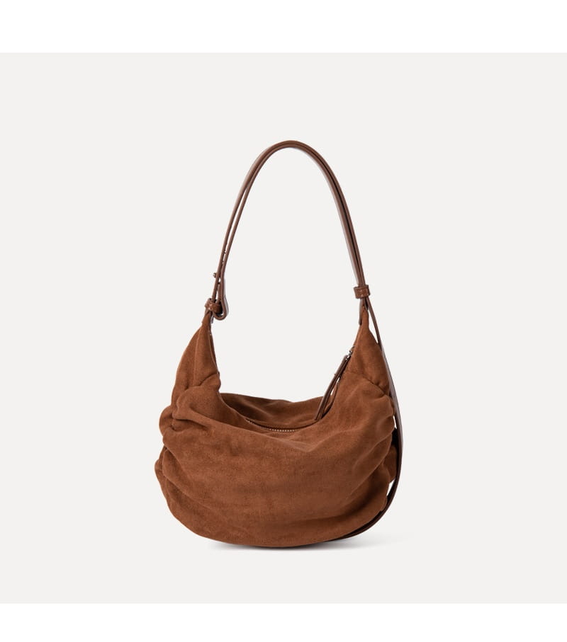 A soft caramel-brown suede dumpling shoulder bag with a gently curved silhouette and matching leather handles designed as a slouchy crossbody hobo.