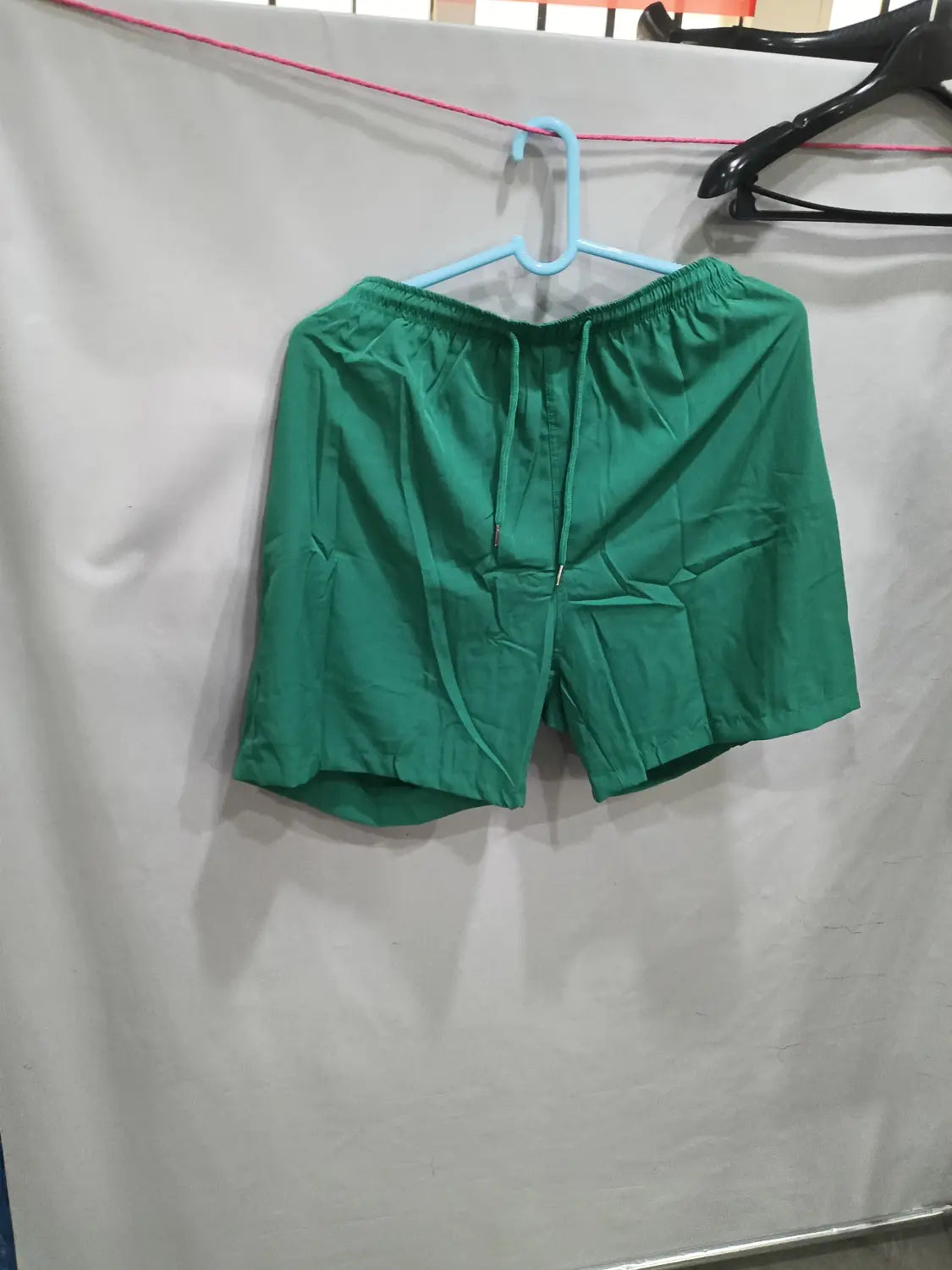 green printed men beach shorts with elastic waistband and drawstring hanging on a blue hanger for summer swim trunks use