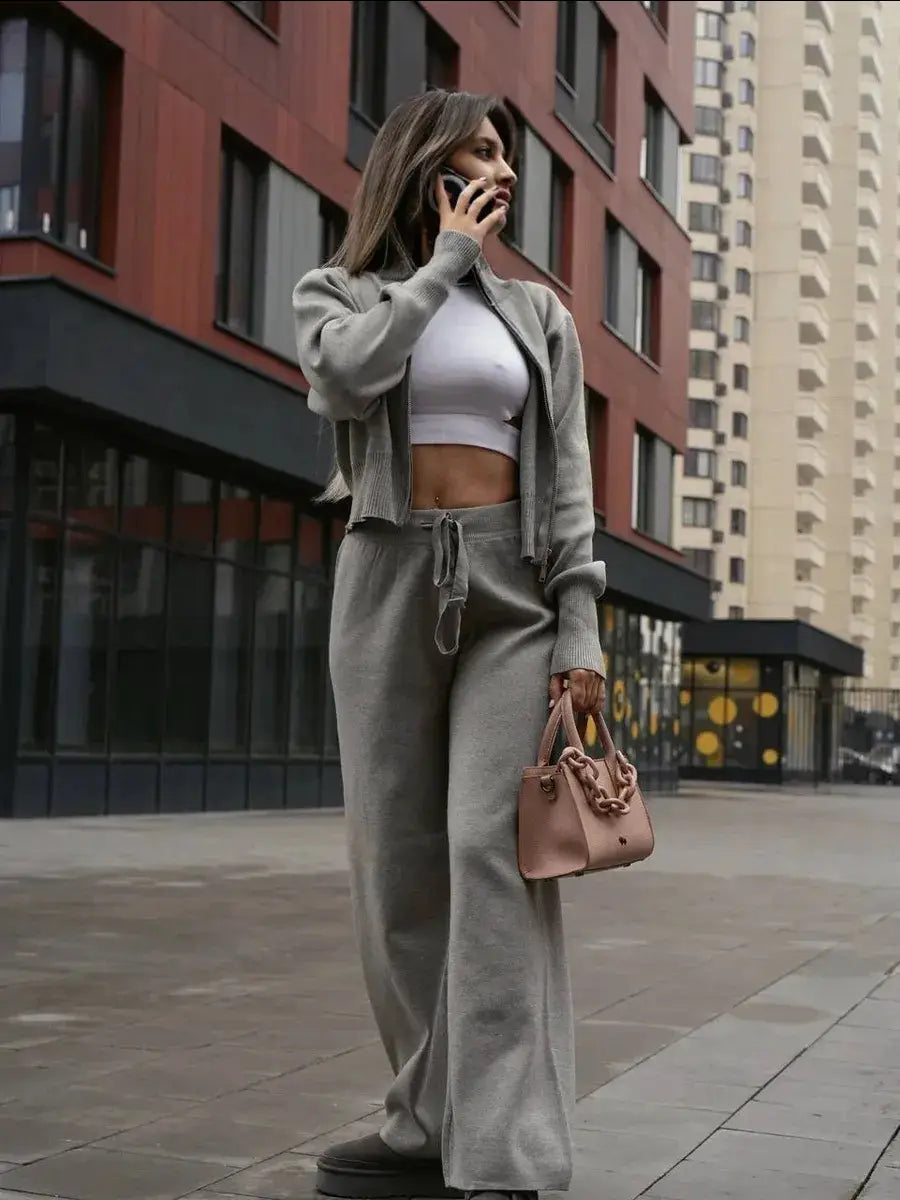 A soft pink handbag with a chunky chain strap complements a women’s knit zip up cardigan and wide leg pant set.