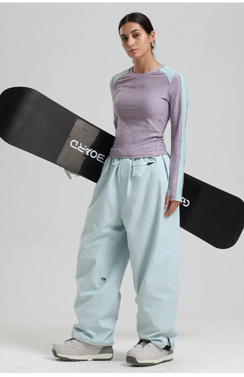 The black snowboard features white lettering and a sleek modern design alongside waterproof windproof black snow pants loose work trousers.