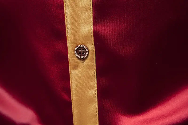 Un botón decorativo con centro negro y borde blanco de cuentas sobre una tapeta dorada de satén de una camisa de manga larga colorblock de satén en tejido rojo intenso