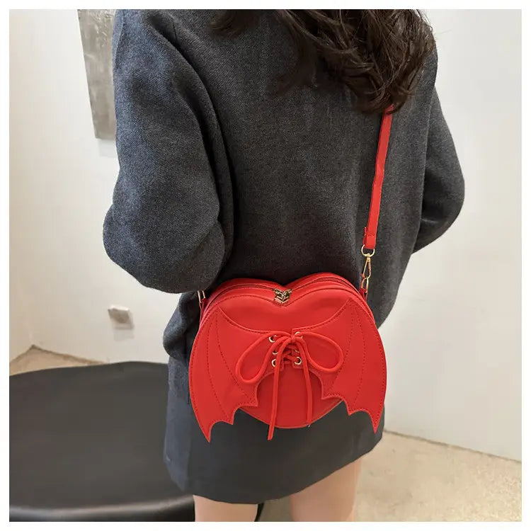 A vibrant red bat wing heart crossbody bag featuring lace-up detail and gold-tone hardware.