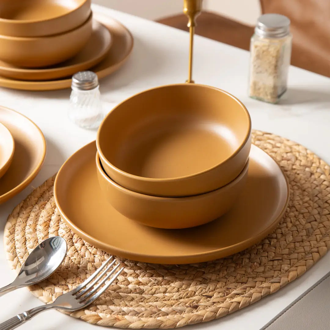 Stoneware dinnerware set 12 piece matte glaze with warm terracotta-colored ceramic bowls stacked neatly on matching plates for four persons.