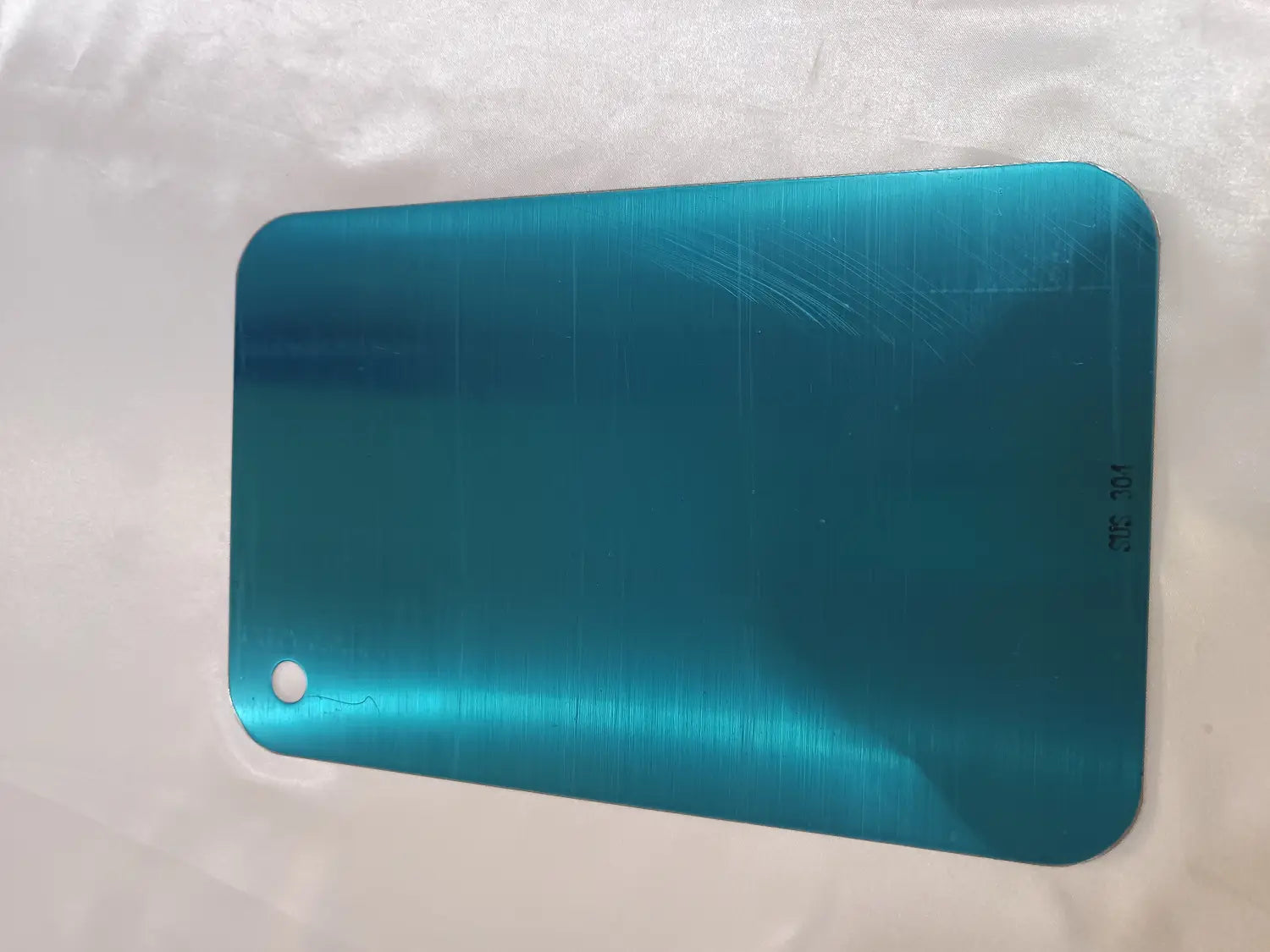 Planche à découper en acier inoxydable métallisé couleur bleu canard avec poignée, présentant un panneau rectangulaire aux coins arrondis et un petit trou pour un usage suspendu anti-moisissure.