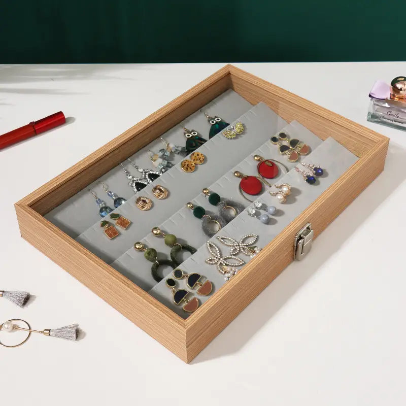 Rosewood jewelry display box with glass lid featuring a light wood rectangular earring organizer with silver latch and gray foam inserts holding various earrings.