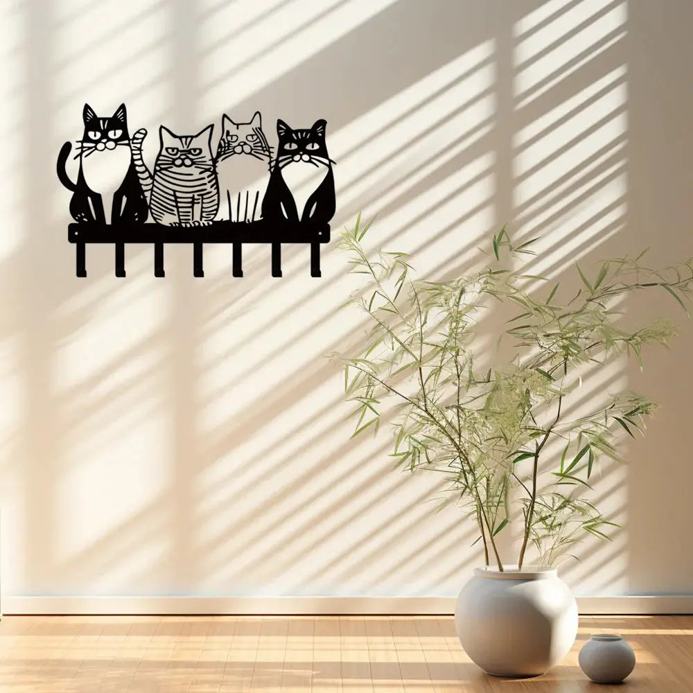 Black metal wall key rack featuring four stylized cats sitting on a bench with four hooks for home decor.
