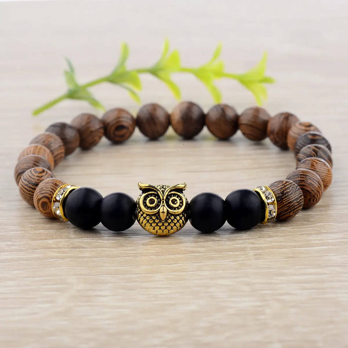 A rustic wooden beaded bracelet featuring a central gold-toned owl charm flanked by black onyx beads and metallic accents.