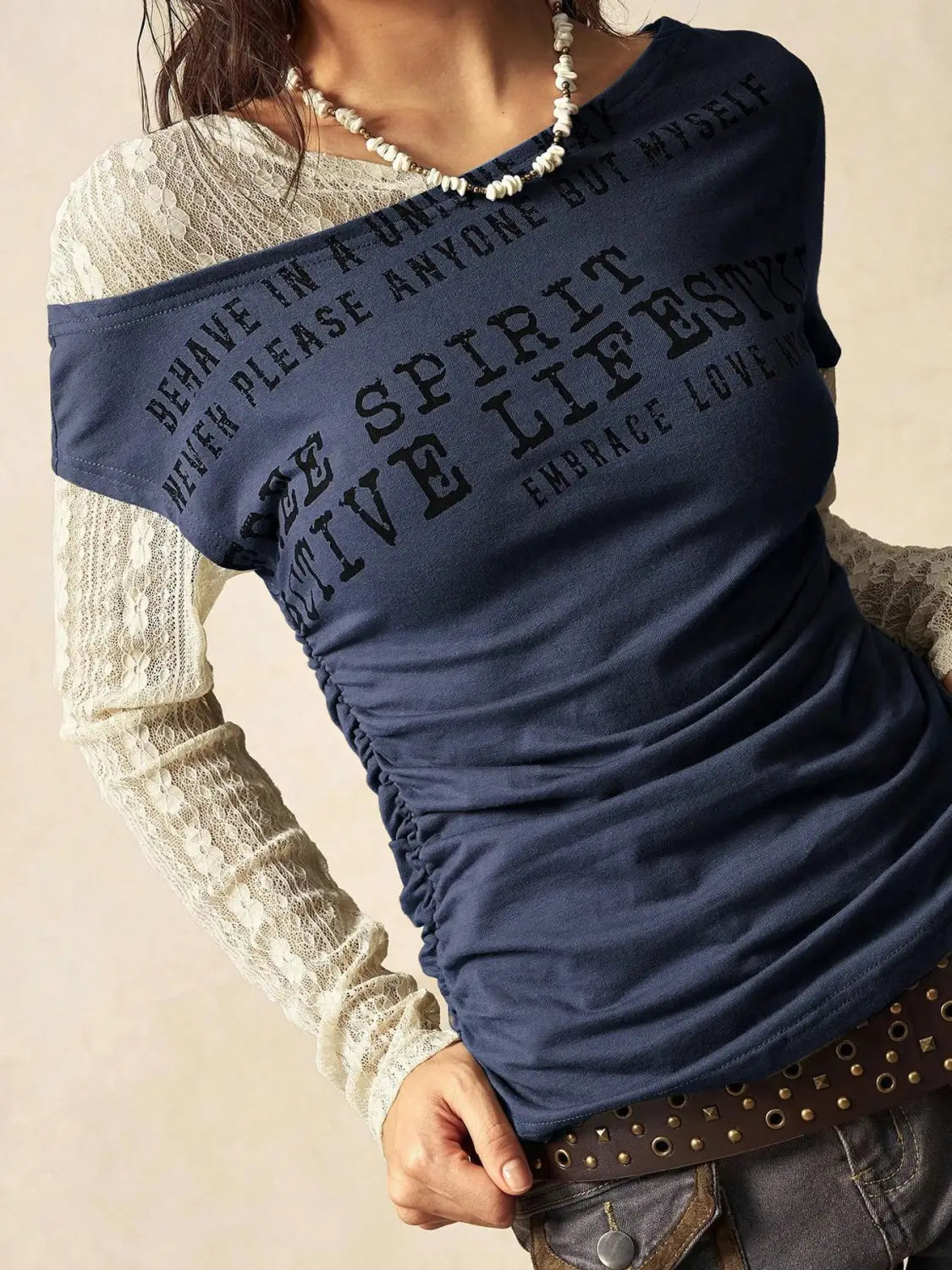 Navy blue off-the-shoulder knitted t-shirt with black printed text and ruched detailing layered over a white lace long-sleeve top in the lace layer off shoulder knitted top product.