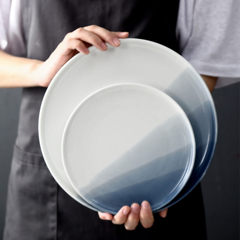 Two ceramic steak plates with a smooth gradient finish transitioning from white to deep blue in a ceramic gradient blue steak plate and bowl set.