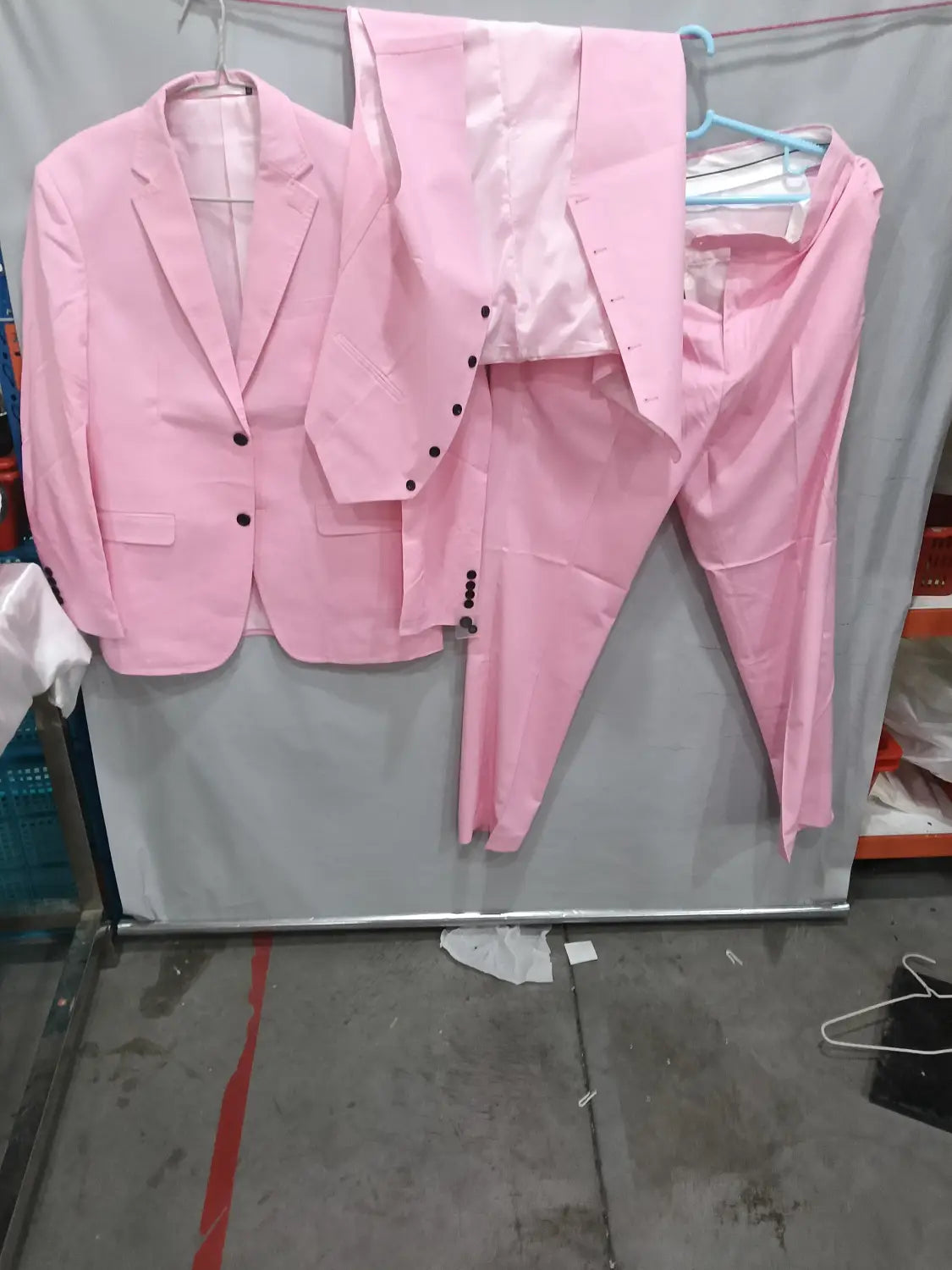 Un costume trois pièces en lin rose pour homme, coupe slim, avec des boutons noirs suspendus sur une corde à linge, pour une tenue décontractée de marié, banquet.