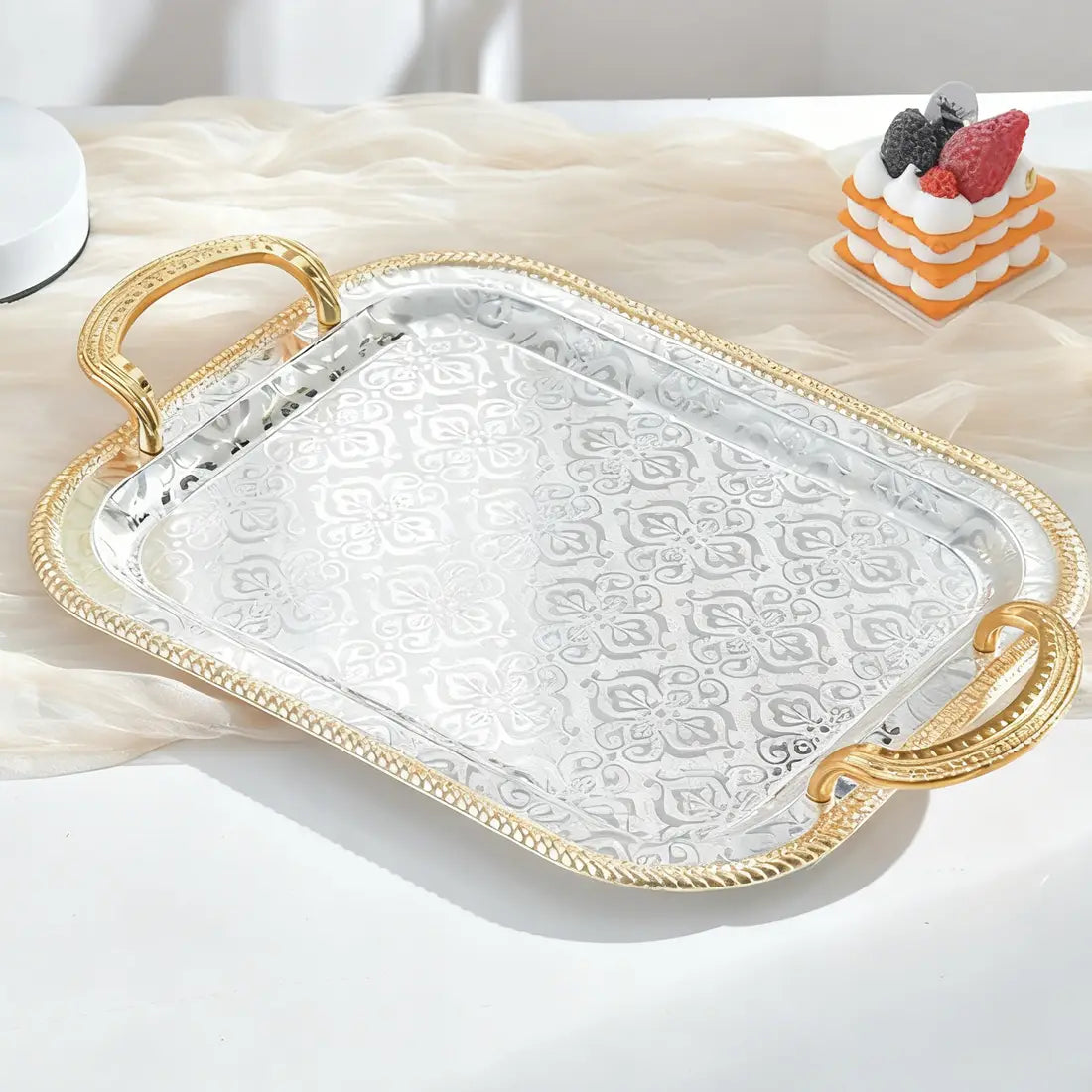 Luxury rectangle serving tray featuring a silver body with a delicate floral pattern etched on its surface and gold-toned ornate handles.