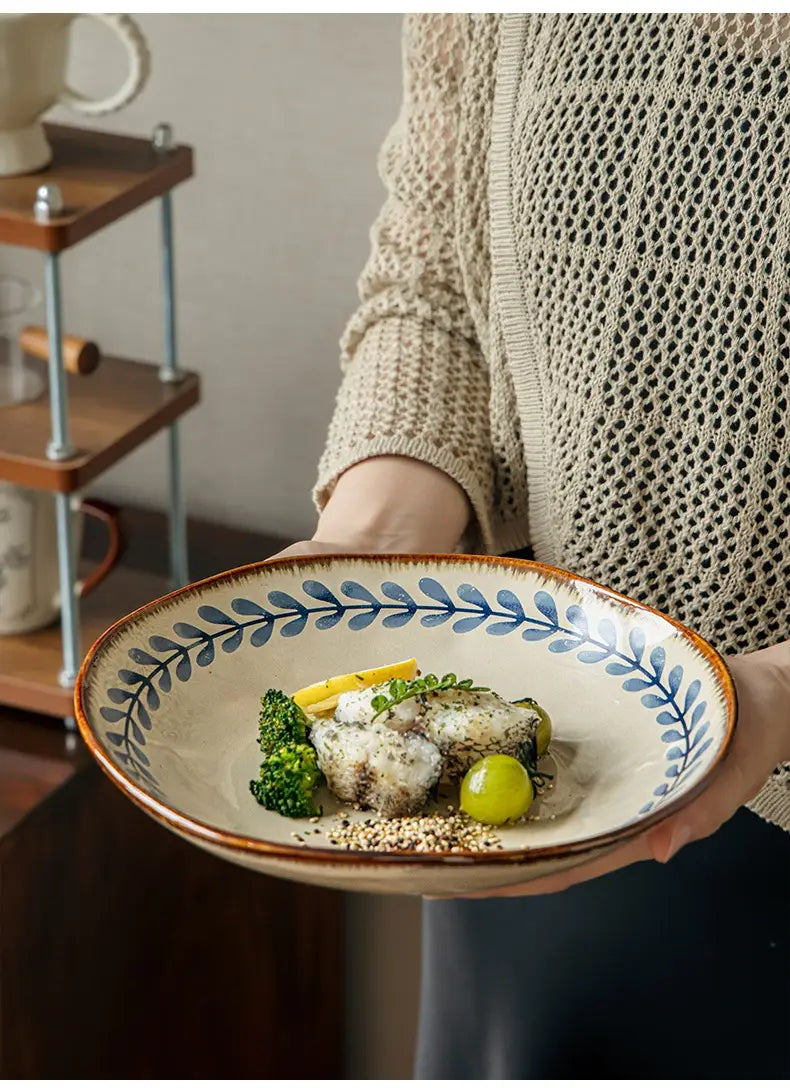 Cream-colored ceramic deep plate with rustic brown rim and delicate blue leaf pattern around the edge measuring 9 inches.