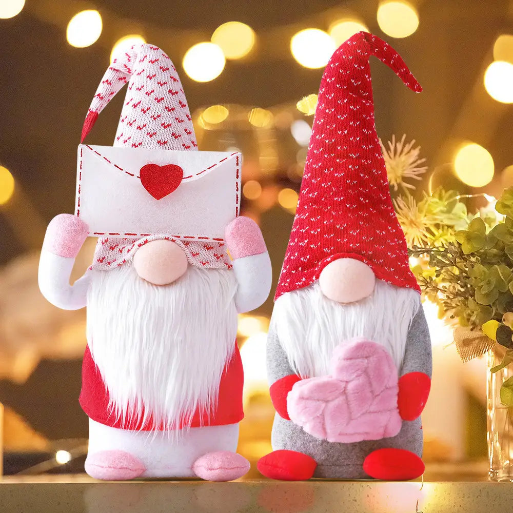 Zwei Plüsch-Valentinsgnom-Puppen, wobei eine eine rote und weiße Strickmütze trägt und einen Herzumschlag hält, und die andere in Grau und Pink ein gestricktes Herz hält; gestaltet als Valentinstag-Gnom-Plüsch, Rudolph-Puppe-Deko-Ornamente.