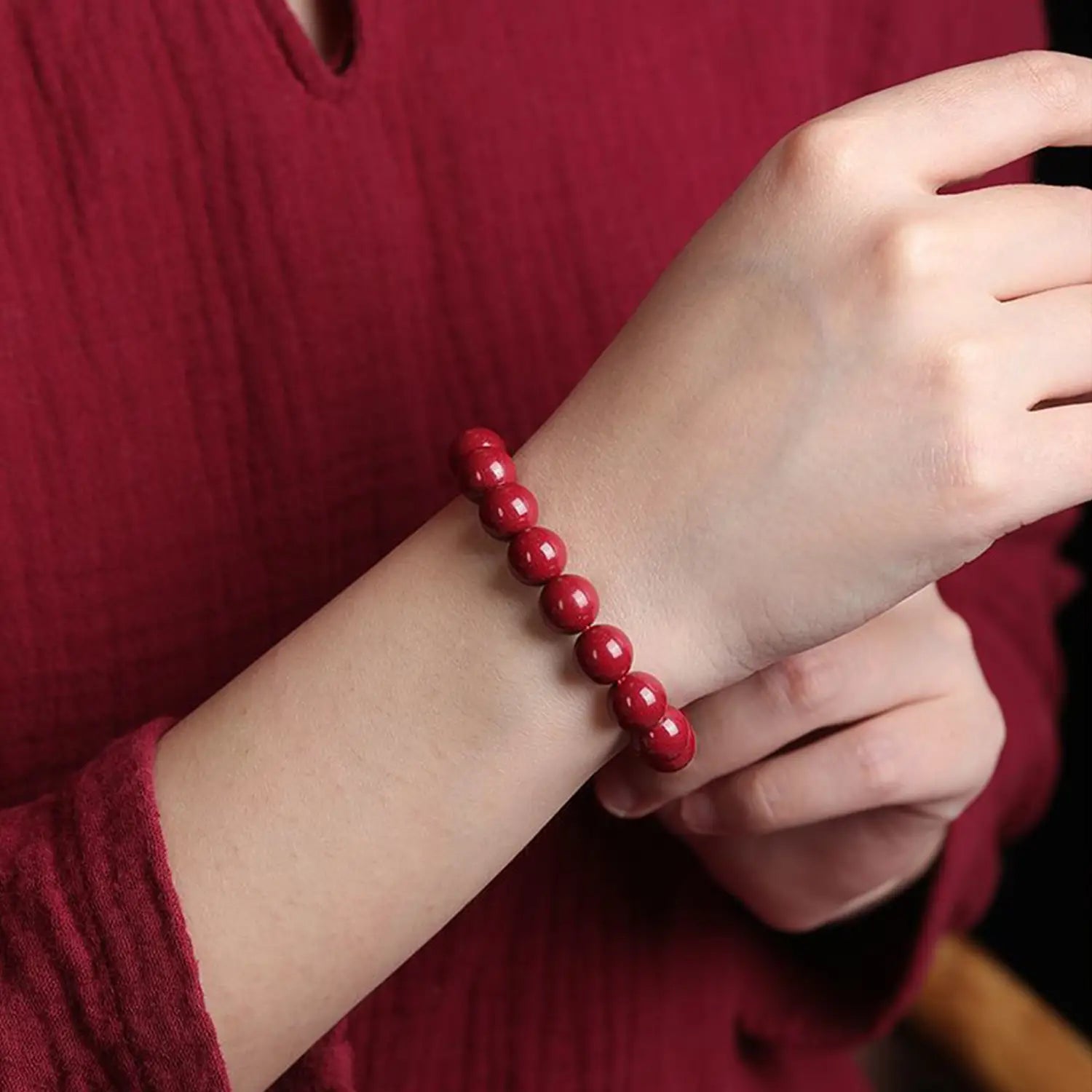 A polished red cinnabar spherical bead bracelet with vibrant glossy beads worn on a wrist.