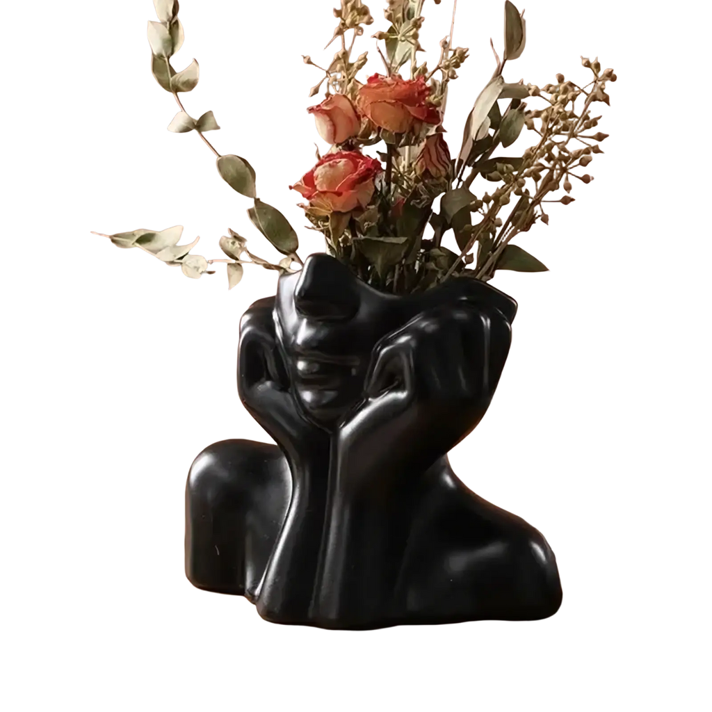 Black ceramic vase shaped like a stylized human bust with hands on cheeks used as an abstract face makeup brush holder