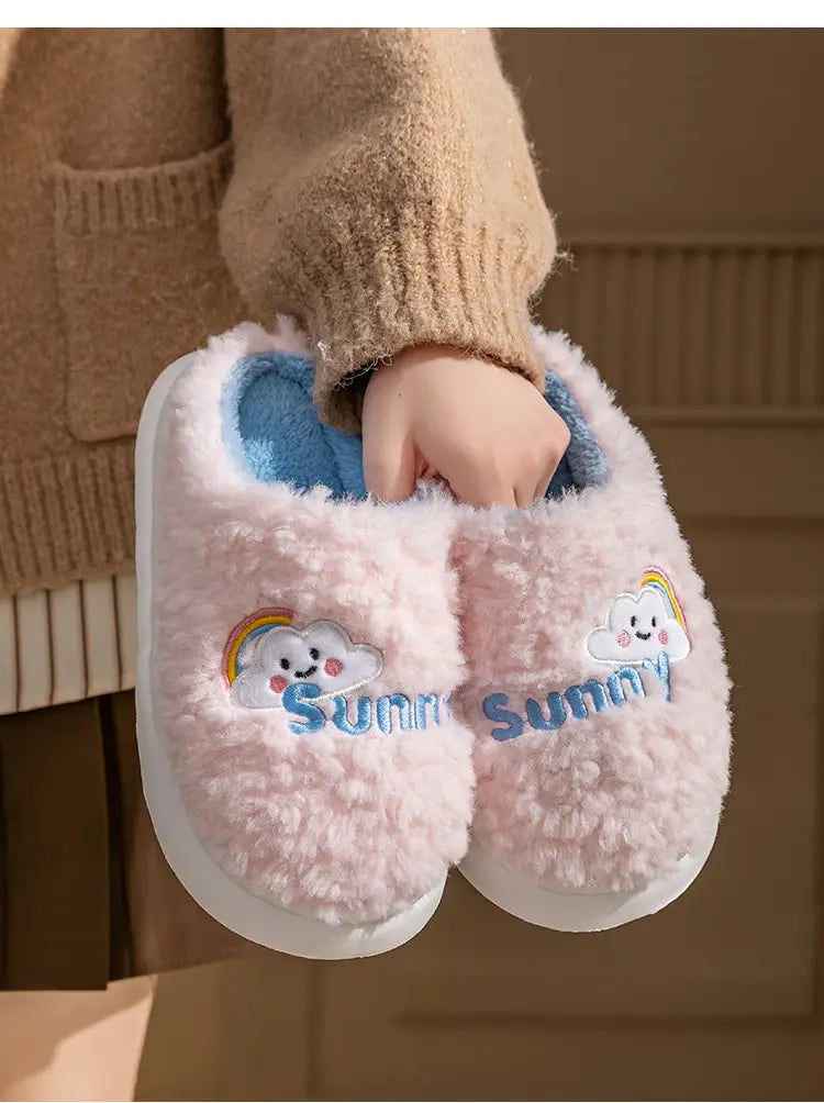pink fluffy plush cotton slippers with embroidered smiling cloud and rainbow design, blue inner lining, and white soles