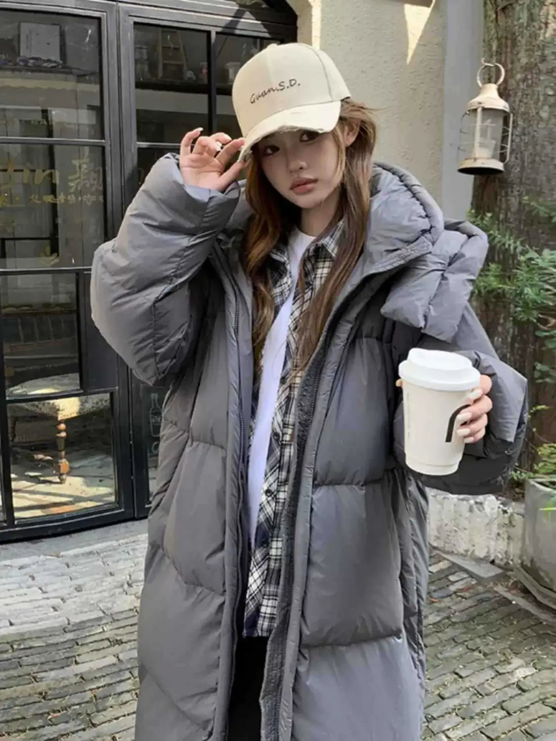 Manteau d’hiver long matelassé et ouaté gris pour femmes, avec capuche et design matelassé, destiné à un usage par temps froid.