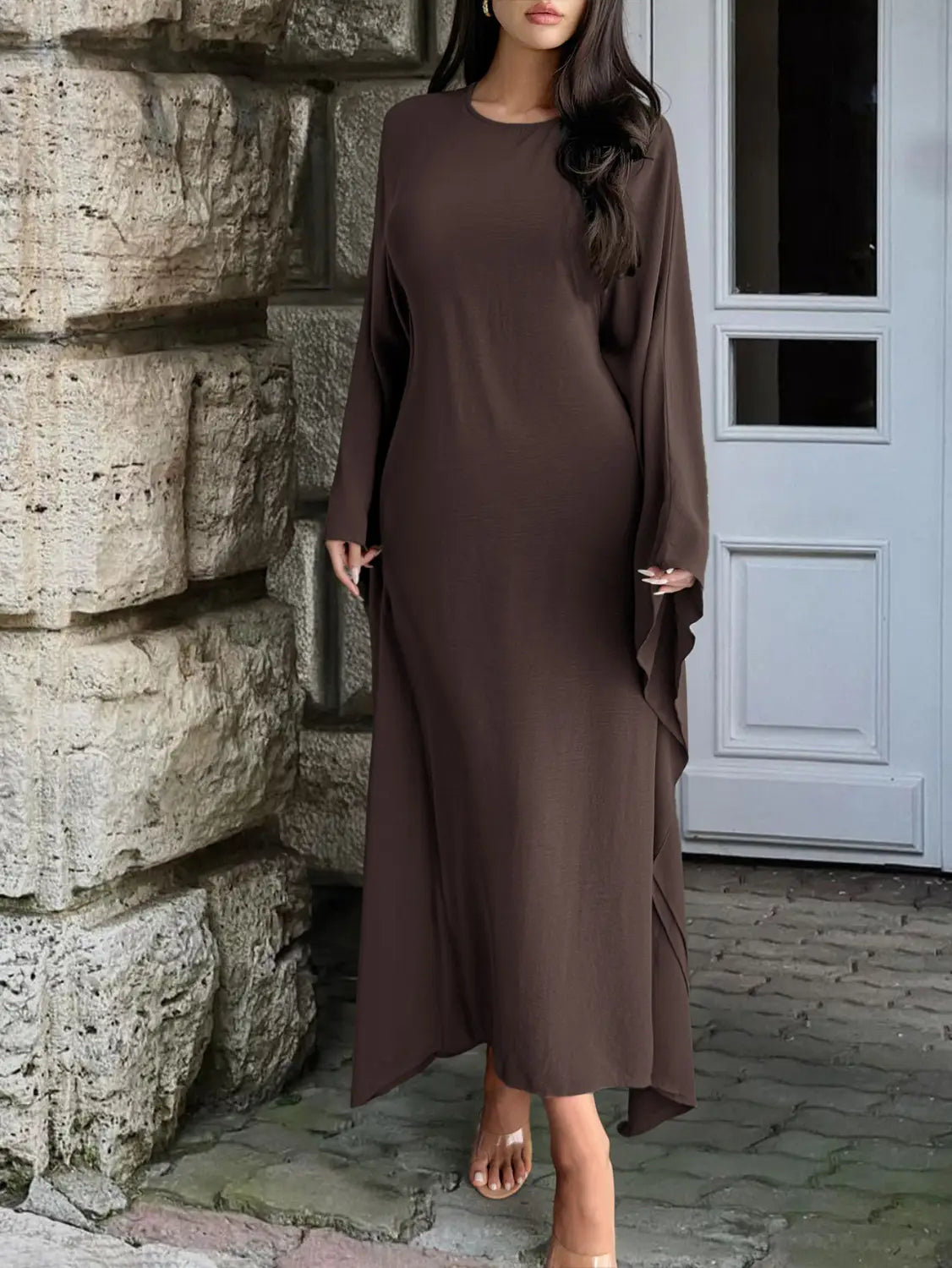 A flowing long-sleeved brown satin maxi dress with a round neckline and asymmetrical ruffled hem.