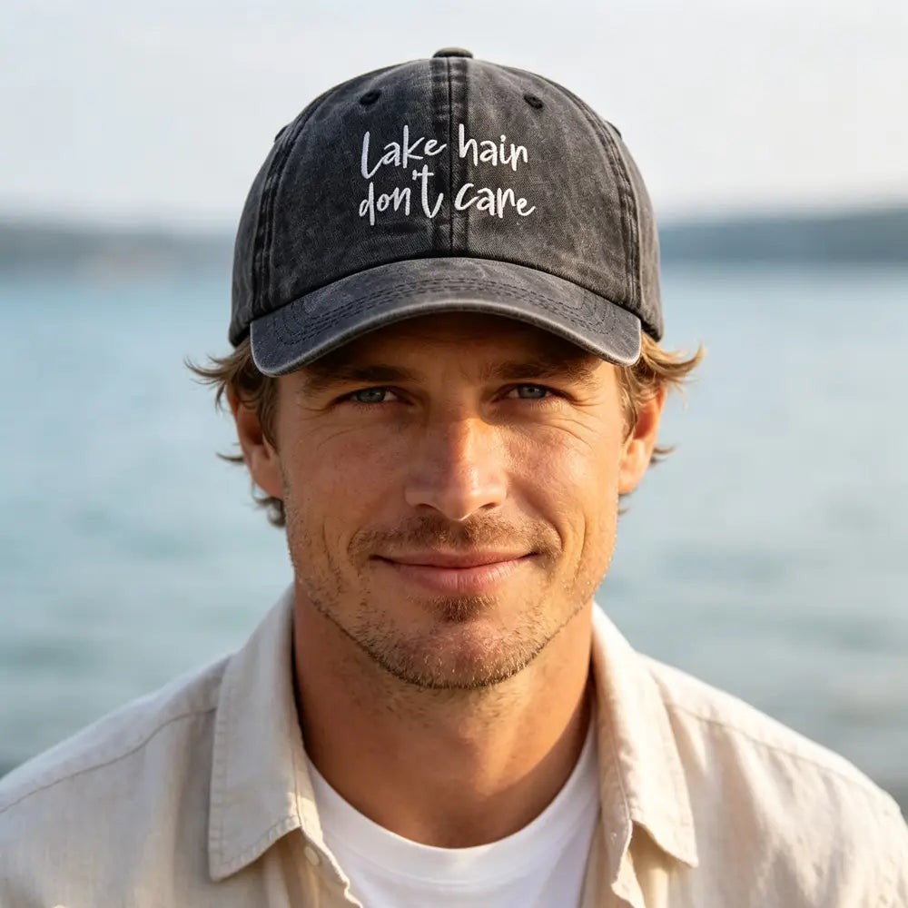 a dark gray distressed baseball cap with white embroidered text lake hair don t care from the lake hair distressed baseball cap set