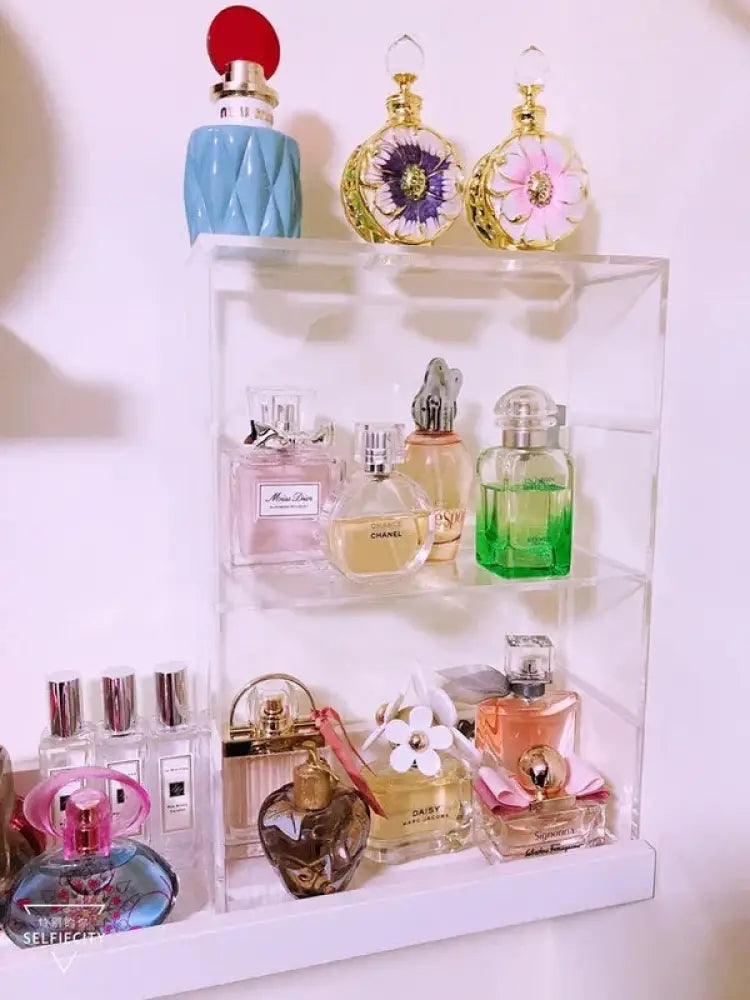 Dustproof clear acrylic stackable makeup organizer with two tiers displaying assorted perfume bottles including blue quilted bottle