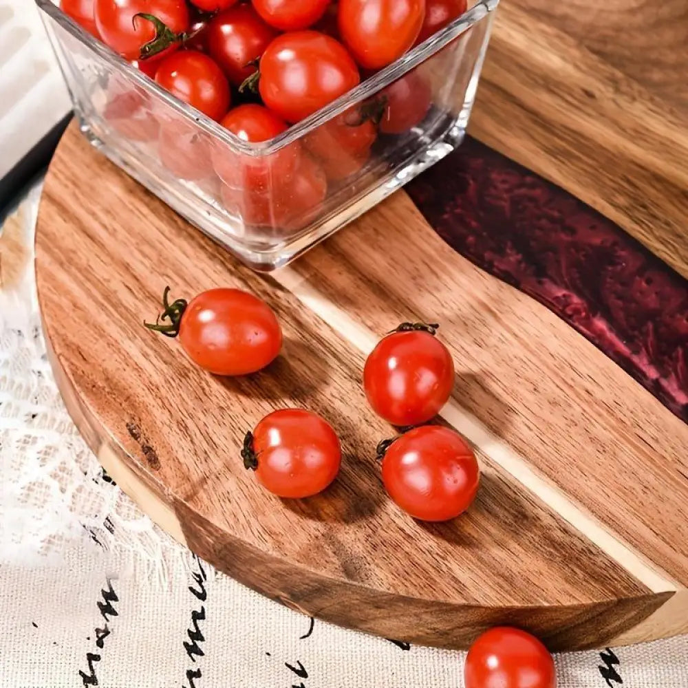 A clear glass square container with red cherry tomatoes on a teal resin river round wooden charcuterie board