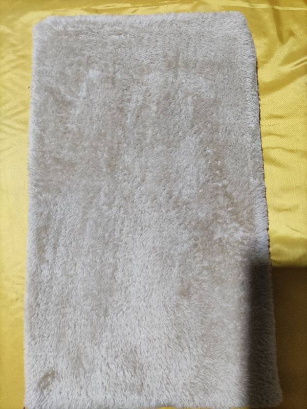 Ein off-weißes, flauschiges rechteckiges Badematten-Accessoire mit weicher, langfloriger Textur zur Verwendung mit der erweiterbaren Katzentransporttasche für Haustiere.