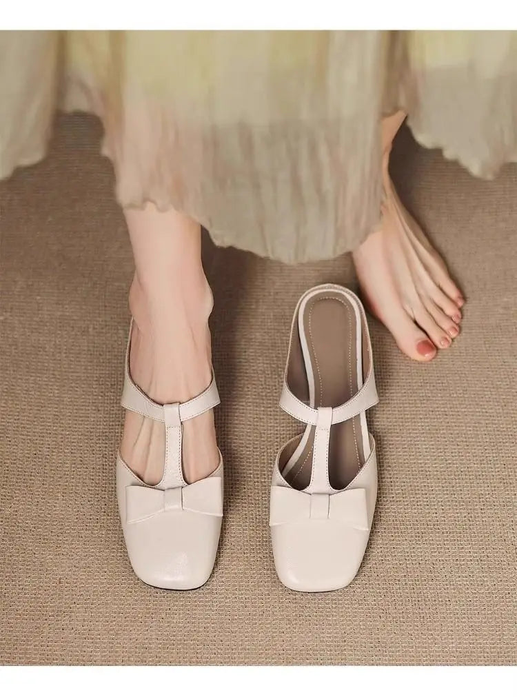 Cream-colored leather bow closed toe mule flats for women with a square toe and t-strap design featuring a glossy finish.