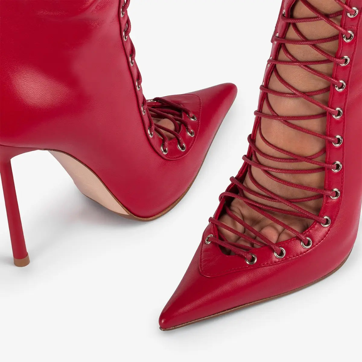 Des bottines à cheville en cuir verni rouge à lacets, avec un talon aiguille à œillet argenté élevé, présentées de l’arrière.