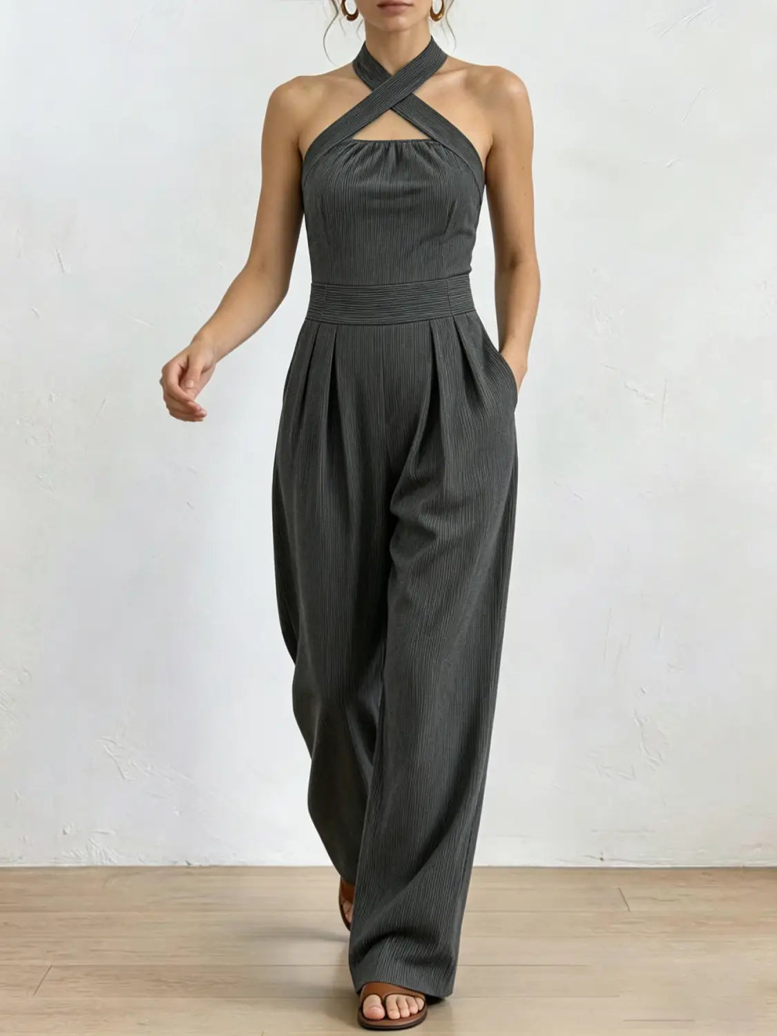 Ein eleganter dunkelgrauer gerippter Halterneck-Jumpsuit mit gekreuztem Frontausschnitt und hoch sitzender plissierter Hose.