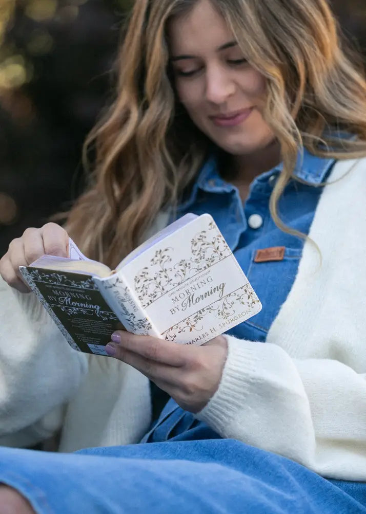 A softcover book titled morning by morning with a white cover and black floral patterns shown alongside an ada denim button front midi dress with belt